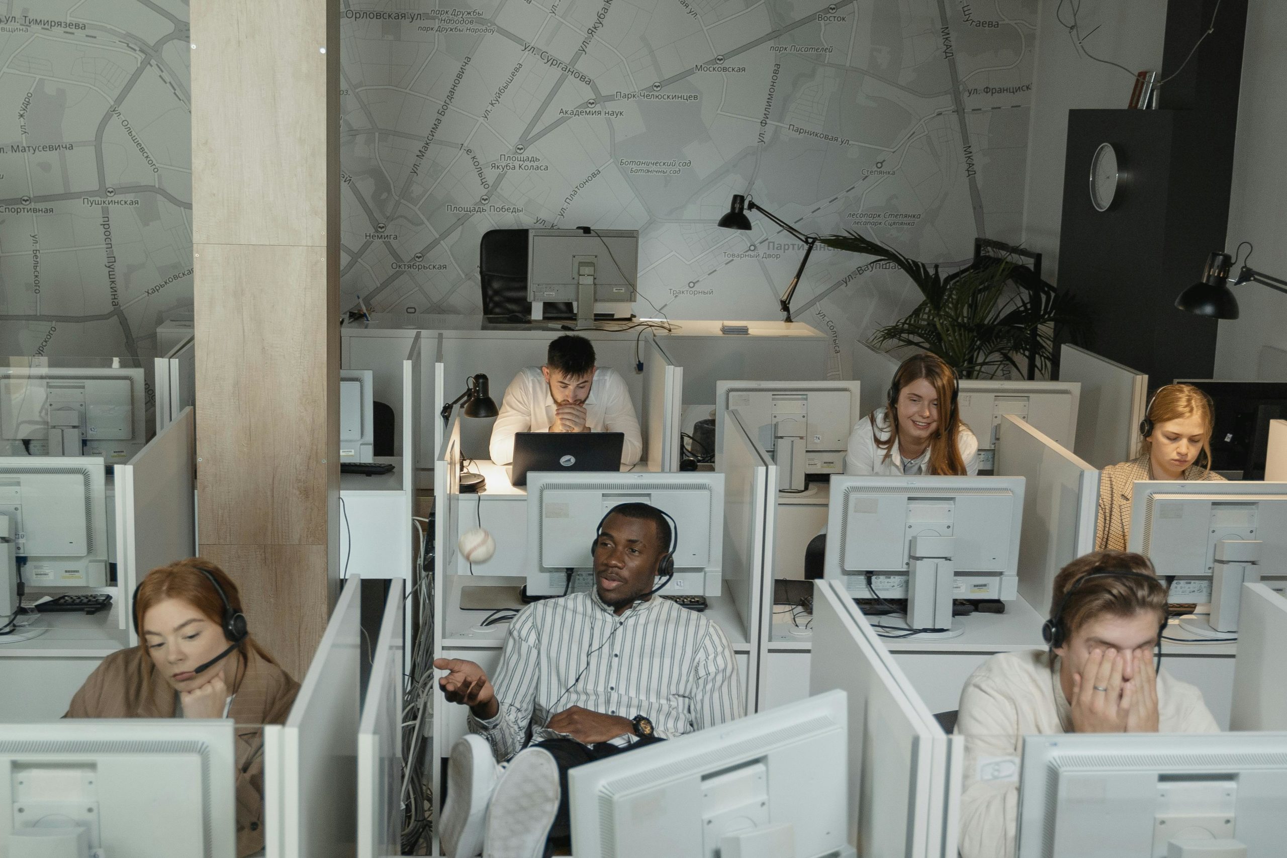 Home A group of diverse call center employees working with computers and headsets in cubicles.